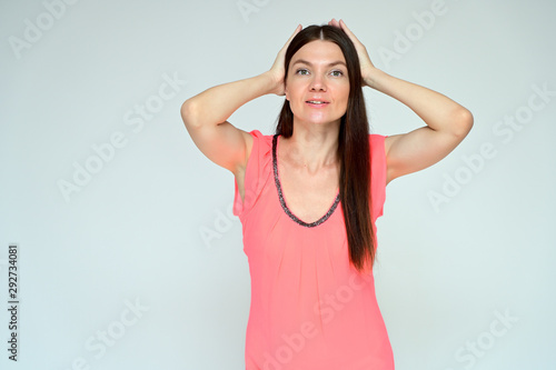 Portrait of a pretty young brunette woman with combed hair on a white background in a pink blouse. It is in different poses. Looks straight at the camera. Slim figure.