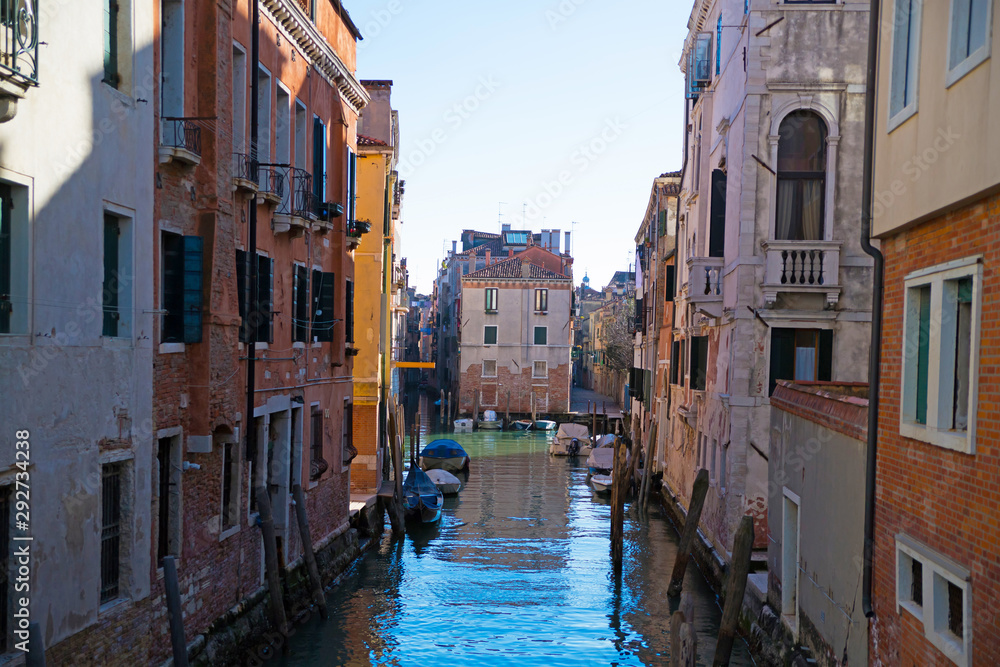 Narrow canal among old colorful brick houses in Venice, Italy.