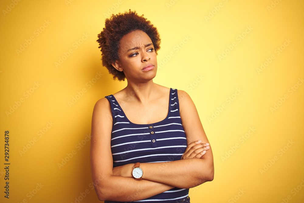 Beauitul african american woman wearing summer t-shirt over isolated yellow background looking to the side with arms crossed convinced and confident Beauitul african american woman wearing summer t-shirt over isolated yellow background looking to the side with arms crossed convinced and confident