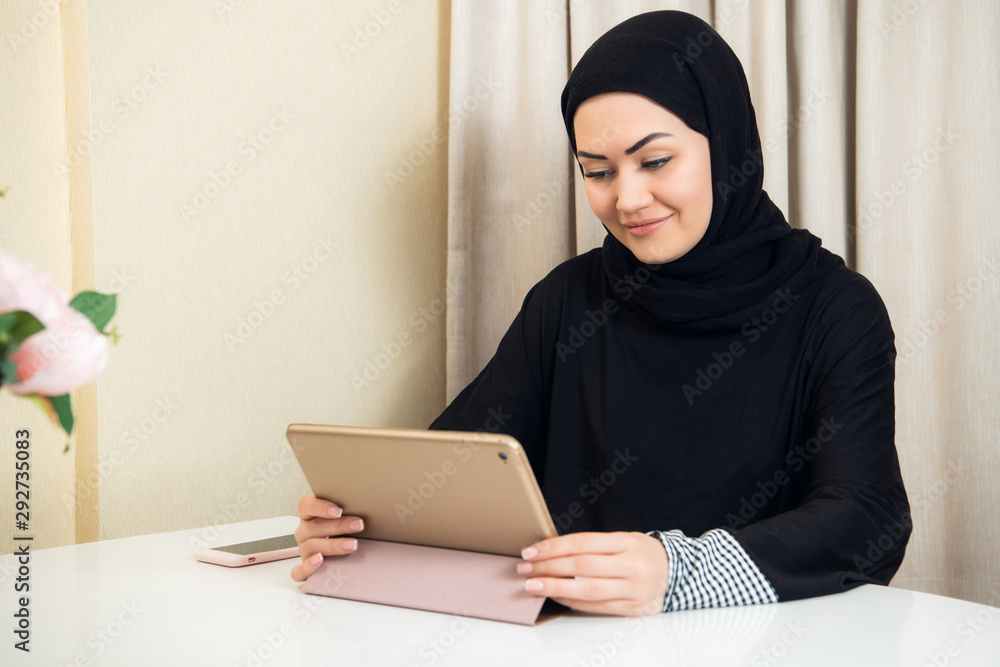 Muslim woman sitting at home with tablet computer, wearing earphones. Rest at home, preparing to watch a film or listen a music. Muslim woman sitting at home with tablet computer, wearing earphones. Rest at home, preparing to watch a film or listen a music.