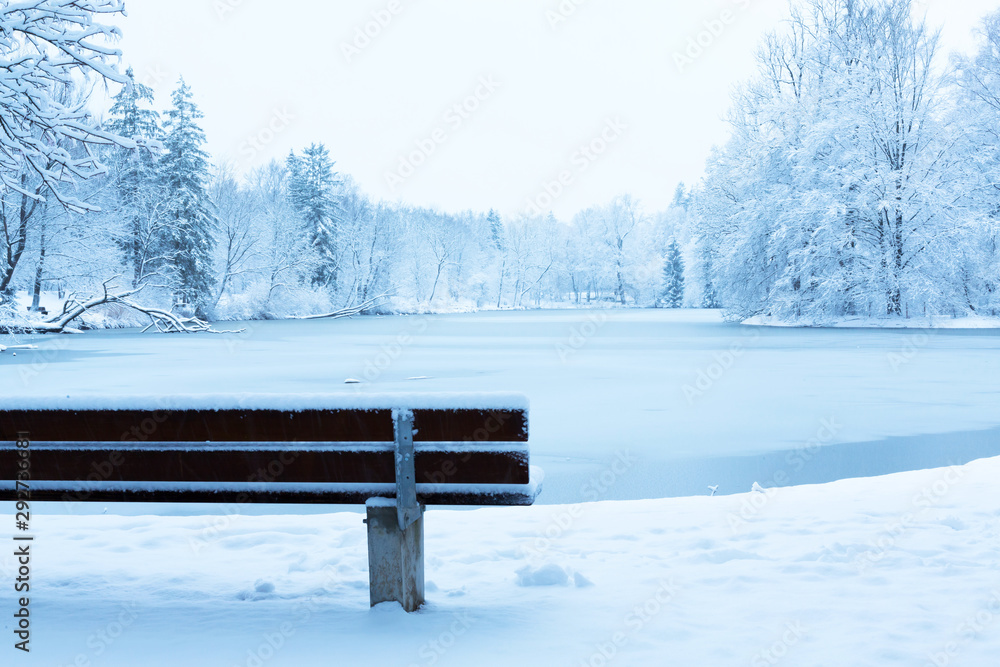 Empty bench in a snowy park near the lake in Munich, Germany
