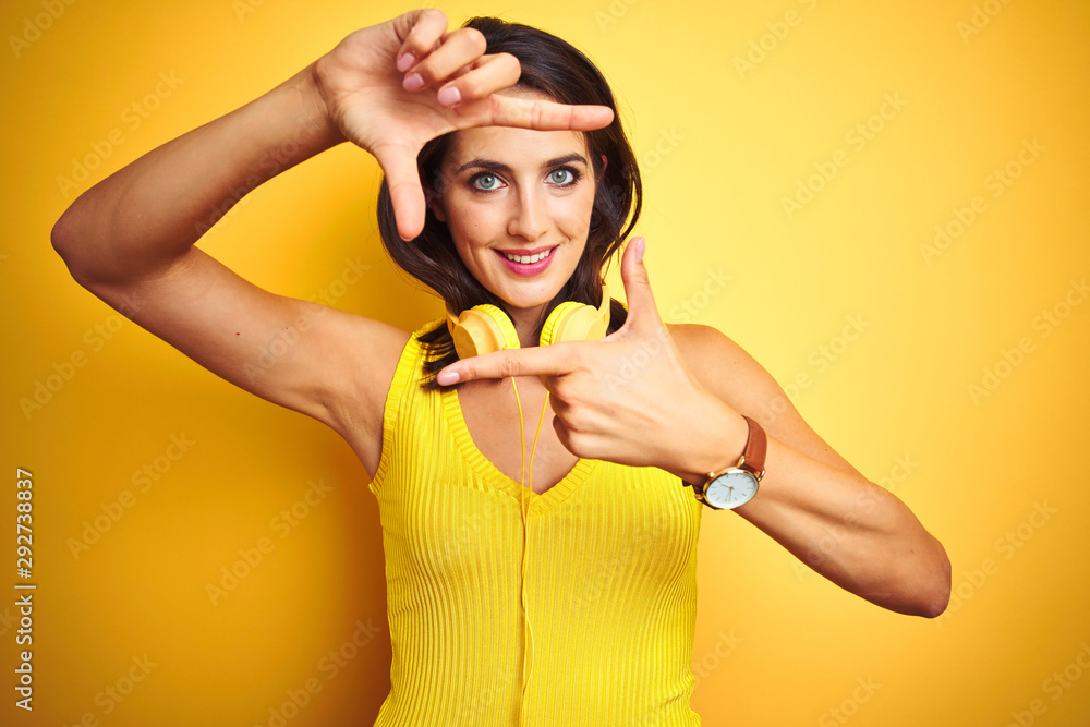 Young beautiful woman wearing headphones over yellow isolated background smiling making frame with hands and fingers with happy face. Creativity and photography concept. Young beautiful woman wearing headphones over yellow isolated background smiling making frame with hands and fingers with happy face. Creativity and photography concept.