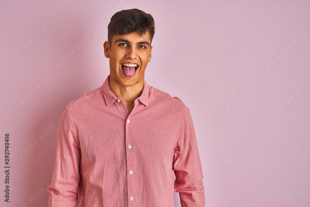 Young indian man wearing elegant shirt standing over isolated pink background sticking tongue out happy with funny expression. Emotion concept. Young indian man wearing elegant shirt standing over isolated pink background sticking tongue out happy with funny expression. Emotion concept.