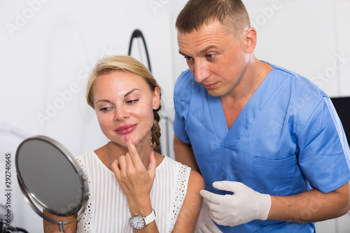 Female patient is analysing her skin with using mirror after the procedure