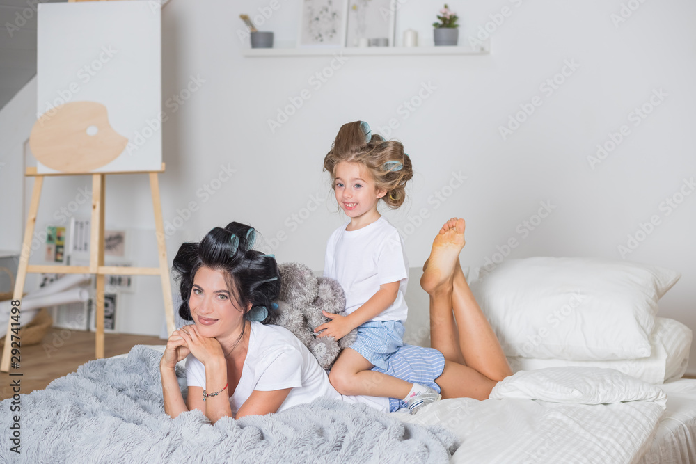 portrait of happy Mother and little daughter in hair curlers.happy mom and daughter having fun on the bed in pajamas.Happy loving family in bedroom in scandinavian style. portrait of happy Mother and little daughter in hair curlers.happy mom and daughter having fun on the bed in pajamas.Happy loving family in bedroom in scandinavian style.