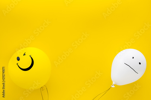 Treat depression concept. Balloons with frustrated and smiling faces on yellow background top view copy space