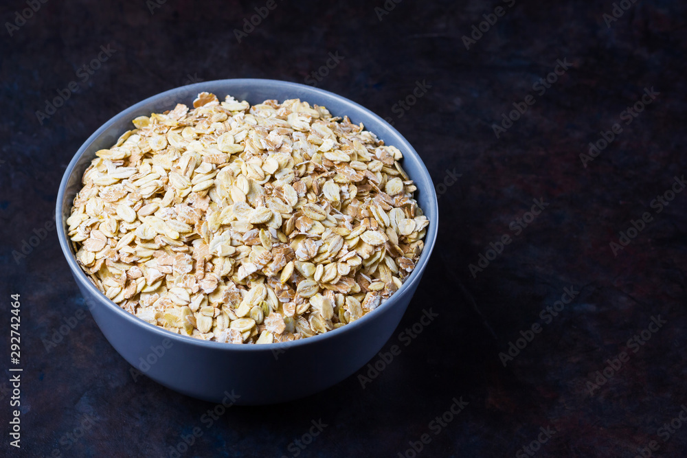 Dry oatmeal in bowl. Oat flakes on dark background. Cereals for making healthy breakfast. Vegetarian food. Copy space Dry oatmeal in bowl. Oat flakes on dark background. Cereals for making healthy breakfast. Vegetarian food. Copy space