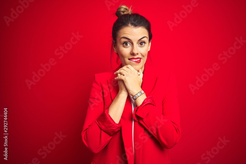 Young beautiful business woman standing over red isolated background laughing nervous and excited with hands on chin looking to the side