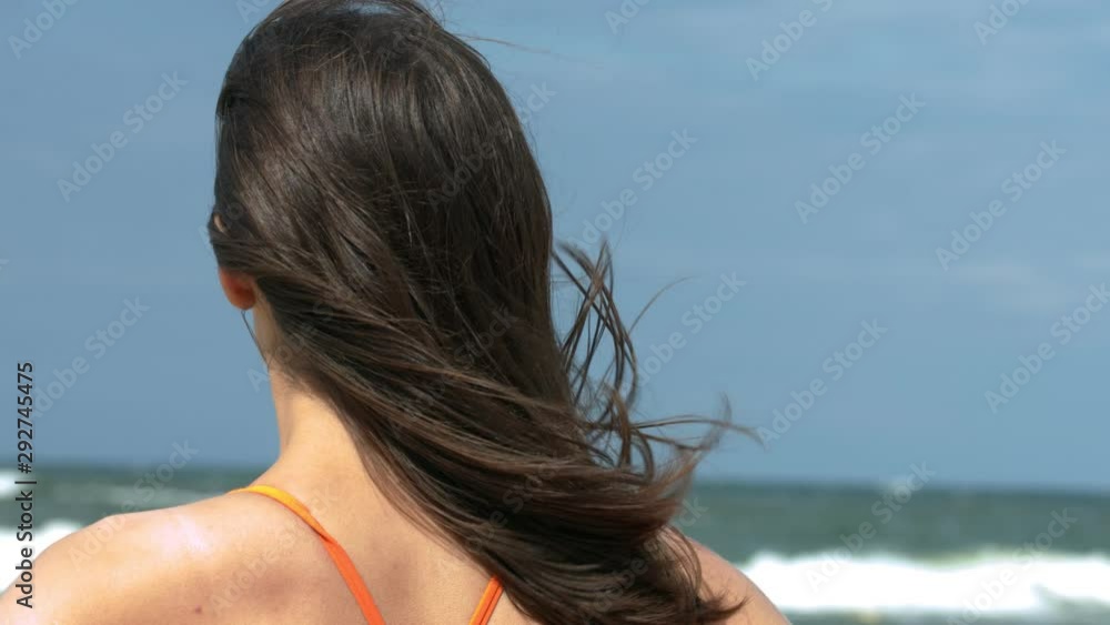 Close-up of a brunette young woman which is stands on the beach and looking out at the wide sea on a sunny day. Close-up of a brunette young woman which is stands on the beach and looking out at the wide sea on a sunny day.