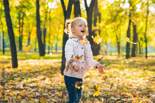 happy little toddler girl throw up maple leaves at autumn public city park