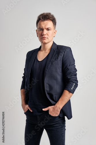 Portrait of serious man in jeans, t-shirt and fitted jacket with hands in pockets over gray background © boomeart