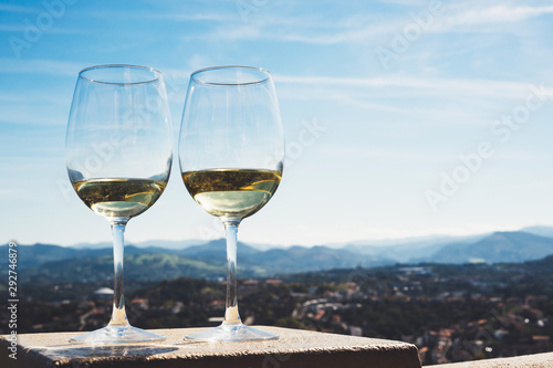 Two drink glass white wine standing on background blue sea top view city coast yacht from observation deck, romantic toast with alcohol panoramic cityscape, spain san sebastian vacation