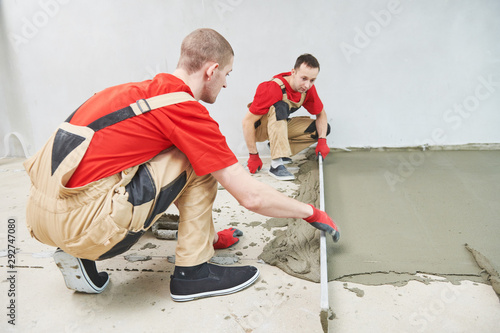 Floor cement work. Plasterer smoothing floor surface with screeder © Kadmy