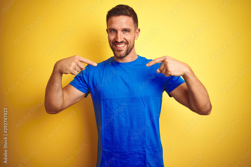 Young handsome man wearing casual blue t-shirt over yellow isolated background looking confident with smile on face, pointing oneself with fingers proud and happy. Young handsome man wearing casual blue t-shirt over yellow isolated background looking confident with smile on face, pointing oneself with fingers proud and happy.