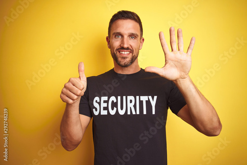 Young safeguard man wearing security uniform over yellow isolated background showing and pointing up with fingers number six while smiling confident and happy. © Krakenimages.com