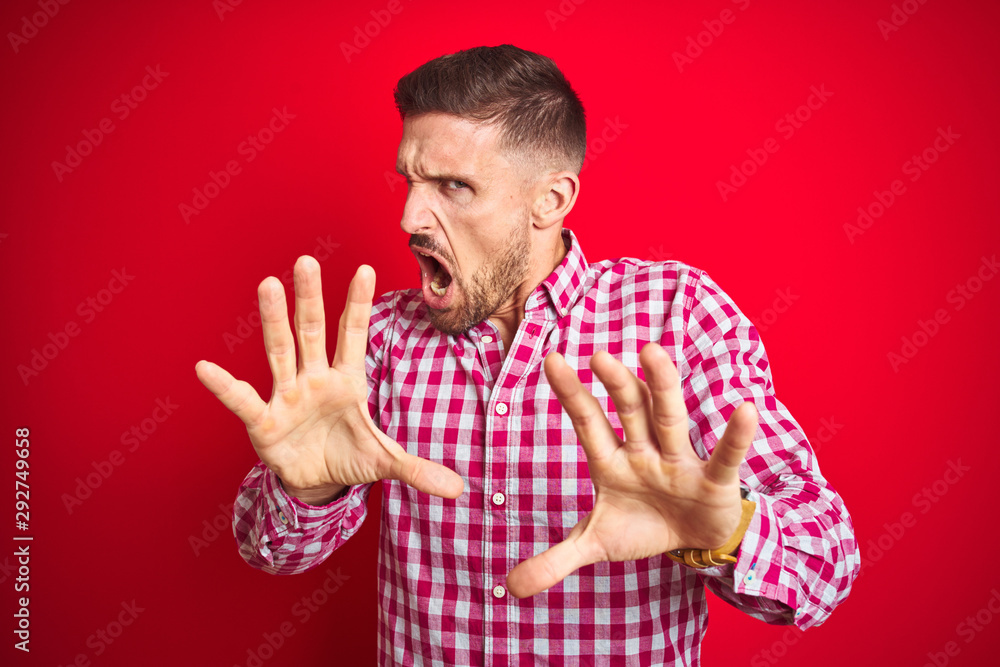 Naklejka premium Young handsome man over red isolated background afraid and terrified with fear expression stop gesture with hands, shouting in shock. Panic concept.