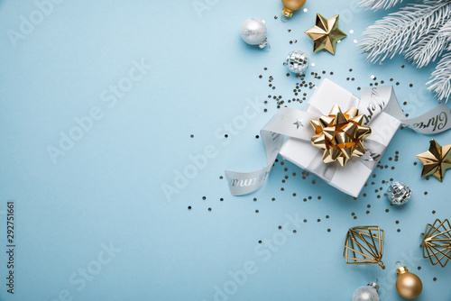 Merry Christmas and Happy Holidays greeting card, frame, banner. New Year. Noel. Christmas white, silver and golden ornaments and gift on blue background top view. Winter xmas holiday theme. Flat lay