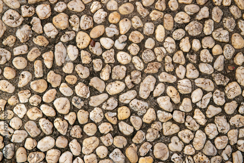 Grungy photo texture of pebble paving  top view background. White pebbles in grey sand top view.