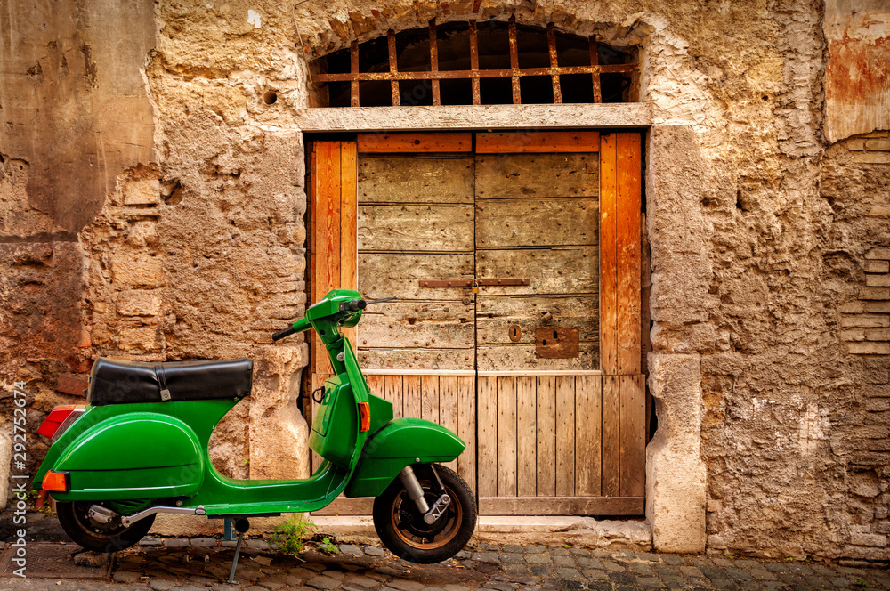 Fototapeta premium Green scooter near an old wall in Rome, Italy. Exterior, architecture and landmark of ancient streets in Rome.