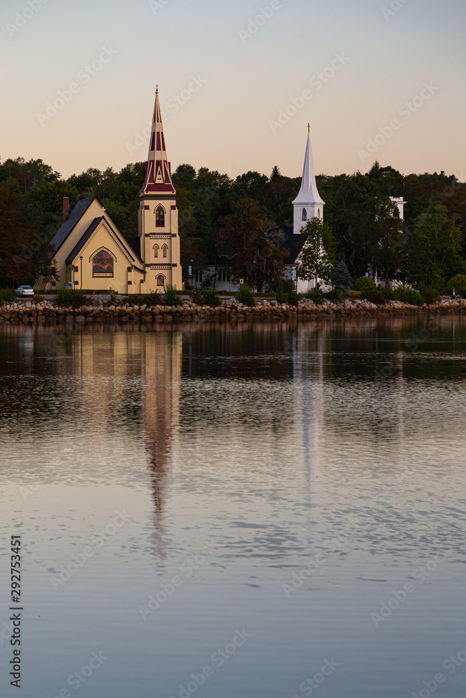 Three churches overlooking Mahone Bay, Nova Scotia, reflected in the water at sunrise.