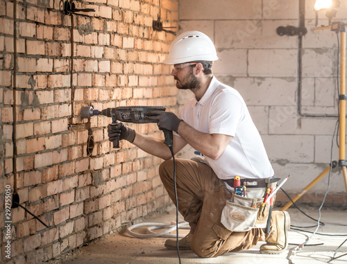 Handyman uses jackhammer, for installation, professional worker on the construction site. The concept of electrician and handyman.