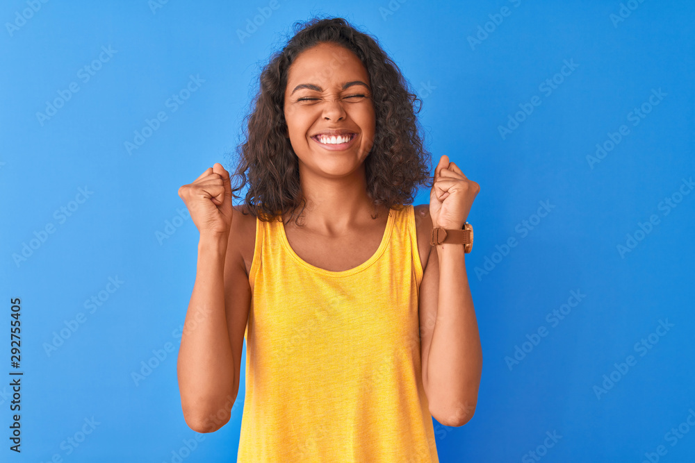 Fototapeta premium Young brazilian woman wearing yellow t-shirt standing over isolated blue background excited for success with arms raised and eyes closed celebrating victory smiling. Winner concept.