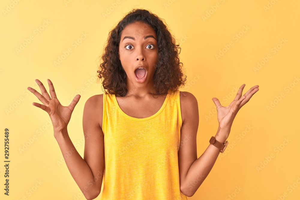 Young brazilian woman wearing t-shirt standing over isolated yellow background celebrating crazy and amazed for success with arms raised and open eyes screaming excited. Winner concept Young brazilian woman wearing t-shirt standing over isolated yellow background celebrating crazy and amazed for success with arms raised and open eyes screaming excited. Winner concept