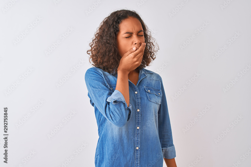 Young brazilian woman wearing denim shirt standing over isolated white background bored yawning tired covering mouth with hand. Restless and sleepiness. Young brazilian woman wearing denim shirt standing over isolated white background bored yawning tired covering mouth with hand. Restless and sleepiness.