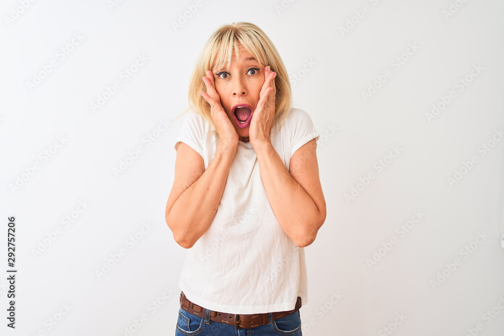 Middle age woman wearing casual t-shirt standing over isolated white background afraid and shocked, surprise and amazed expression with hands on face Middle age woman wearing casual t-shirt standing over isolated white background afraid and shocked, surprise and amazed expression with hands on face