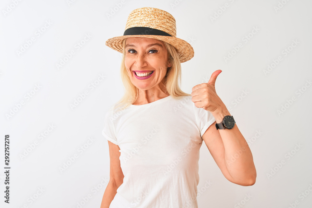 Middle age woman wearing casual t-shirt and hat standing over isolated white background doing happy thumbs up gesture with hand. Approving expression looking at the camera with showing success. Middle age woman wearing casual t-shirt and hat standing over isolated white background doing happy thumbs up gesture with hand. Approving expression looking at the camera with showing success.