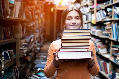 girl student holds a stack of books in the library, she searches for literature and offers to read, a woman prepares for study, knowledge is power, bookseller on the background of the bookstore