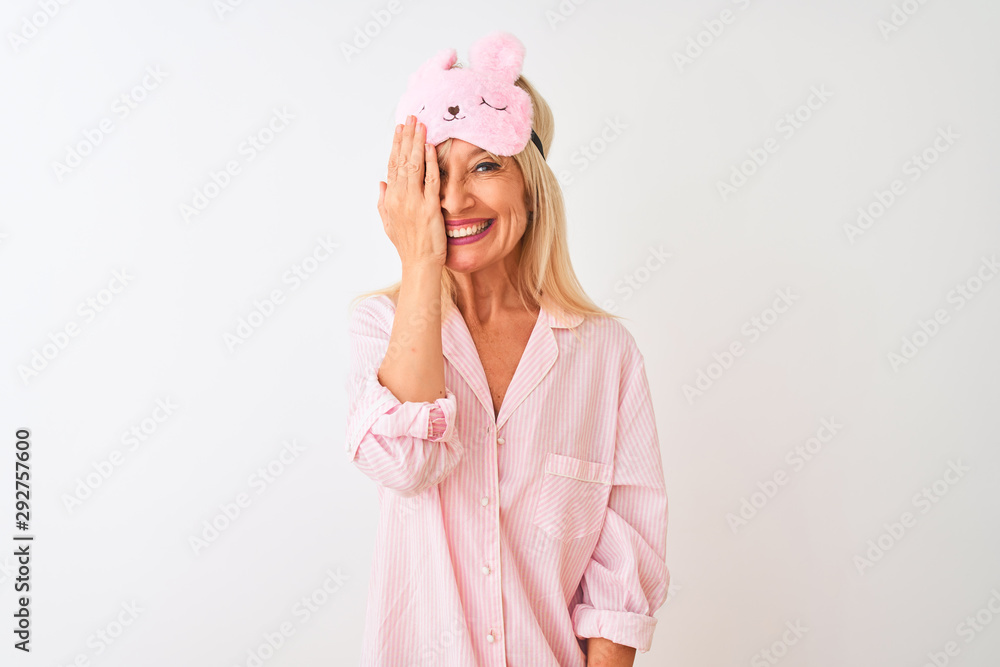 Middle age woman wearing sleep mask and pajama over isolated white background covering one eye with hand, confident smile on face and surprise emotion. Middle age woman wearing sleep mask and pajama over isolated white background covering one eye with hand, confident smile on face and surprise emotion.