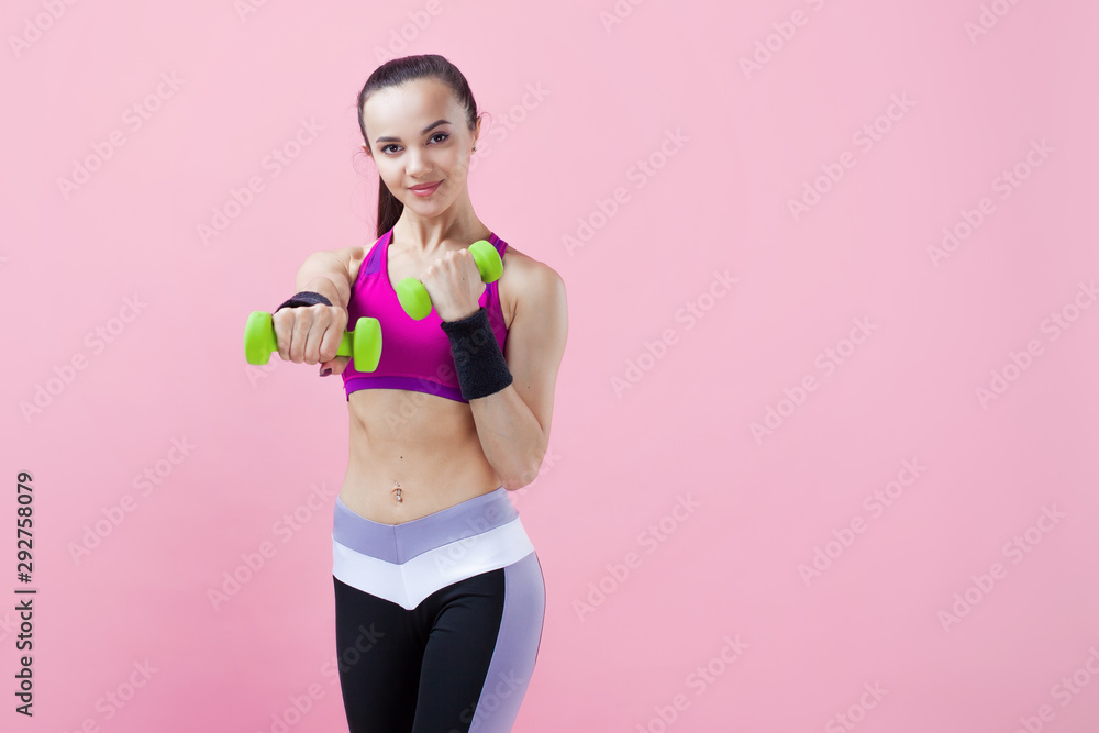 Young athletic woman, with a smile, in a bright top, trains punches, keeps dumbbells on weight, on a pink background. Young athletic woman, with a smile, in a bright top, trains punches, keeps dumbbells on weight, on a pink background.