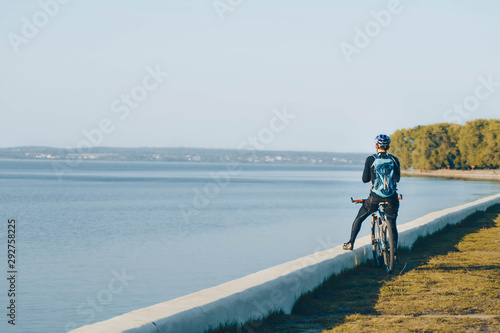 man cyclist riding bicycle on free road near lake and enjoying view. healthy lifestyle, welness concept. back view.