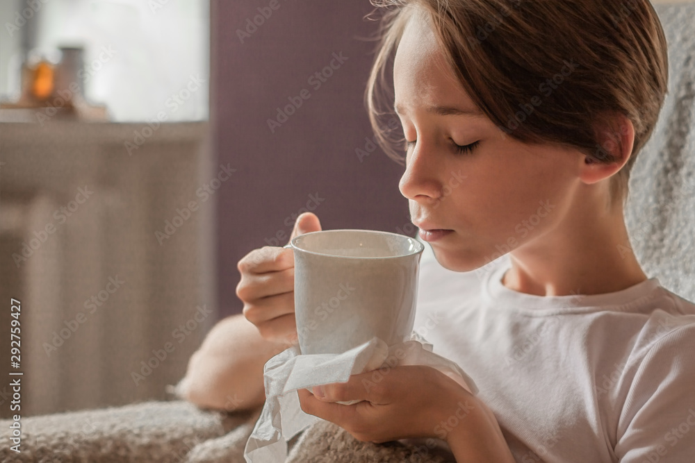 The boy is sick. A child wrapped in a blanket with a mug of medicine, has the flu at home The boy is sick. A child wrapped in a blanket with a mug of medicine, has the flu at home