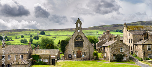 Panorama of green pastureland for sheep with drystone walls behind Congregational Church and stone cottages in Reeth North Yorkshire England photo