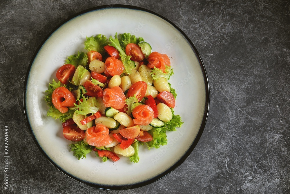 Healthy potato gnocchi salad with cherry tomatoes, cucumber, bell pepper, slightly salted salmon, olive oil and lettuce. Top view. Healthy potato gnocchi salad with cherry tomatoes, cucumber, bell pepper, slightly salted salmon, olive oil and lettuce. Top view.
