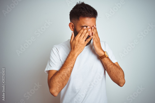 Fotografie Young indian man wearing t-shirt standing over isolated white background rubbing eyes for fatigue and headache, sleepy and tired expression
