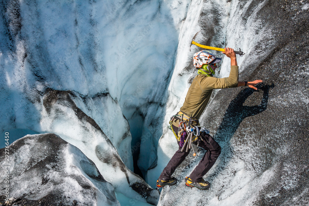 Obraz premium Young man solo ice climbing a short gradual slope next to a large ice cave.