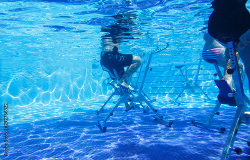 Fitness class doing aqua aerobics on exercise bikes in swimming pool resort hotel