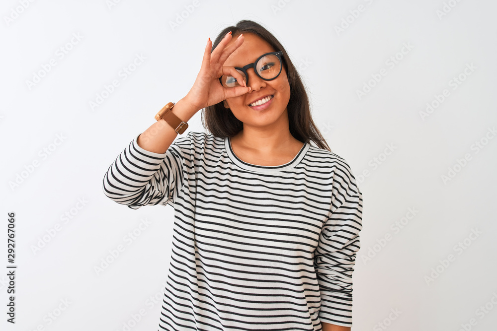 Young chinese woman wearing striped t-shirt and glasses over isolated white background doing ok gesture with hand smiling, eye looking through fingers with happy face. Young chinese woman wearing striped t-shirt and glasses over isolated white background doing ok gesture with hand smiling, eye looking through fingers with happy face.