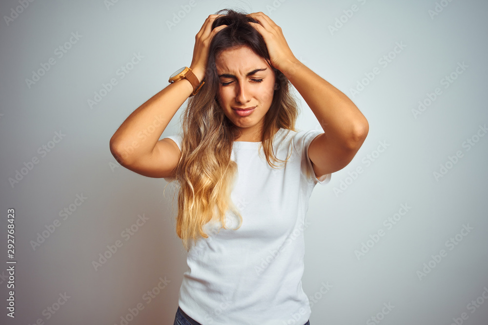 Young beautiful woman wearing casual white t-shirt over isolated background suffering from headache desperate and stressed because pain and migraine. Hands on head. Young beautiful woman wearing casual white t-shirt over isolated background suffering from headache desperate and stressed because pain and migraine. Hands on head.