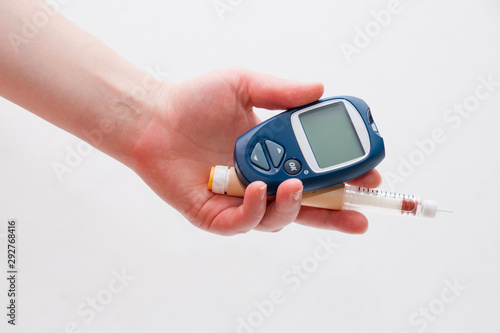 female hand holds a blue glucometer and a syringe for diabetes insulin injection pen