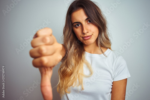 Young beautiful woman wearing t-shirt over white isolated background with angry face, negative sign showing dislike with thumbs down, rejection concept