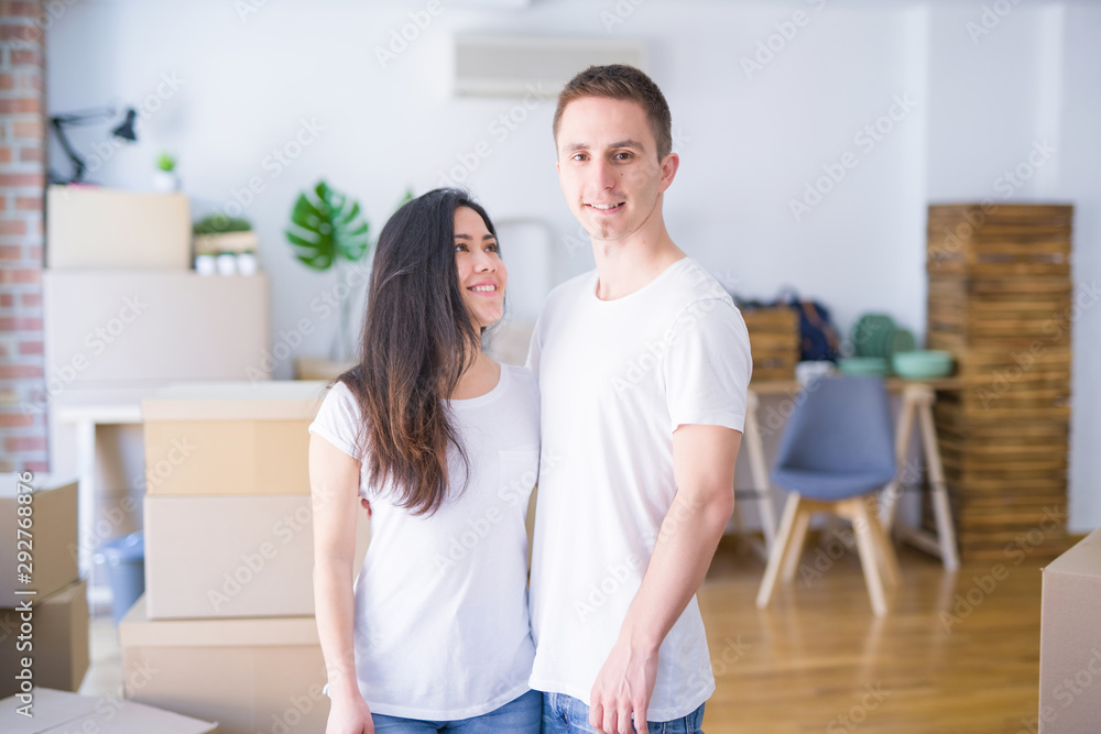 Fototapeta premium Young beautiful couple standing at new home around cardboard boxes