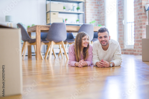 Young beautiful couple in love moving to new home, lying on the floor around cardboard boxes, very happy and cheerful for new apartment