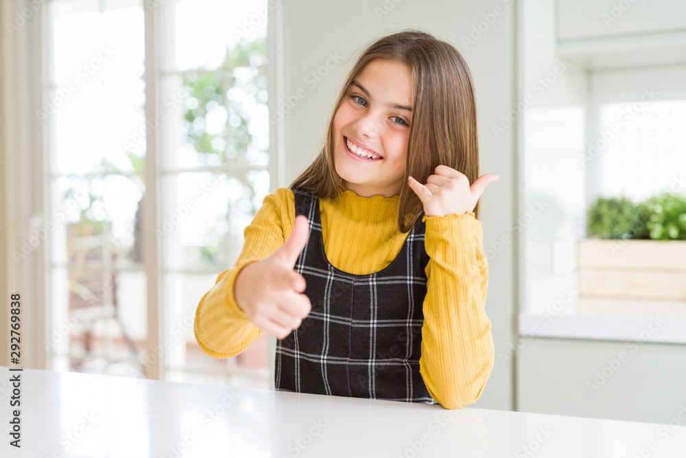 Young beautiful blonde kid girl wearing casual yellow sweater at home smiling doing talking on the telephone gesture and pointing to you. Call me.