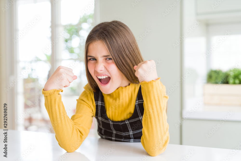 Young beautiful blonde kid girl wearing casual yellow sweater at home angry and mad raising fists frustrated and furious while shouting with anger. Rage and aggressive concept. Young beautiful blonde kid girl wearing casual yellow sweater at home angry and mad raising fists frustrated and furious while shouting with anger. Rage and aggressive concept.