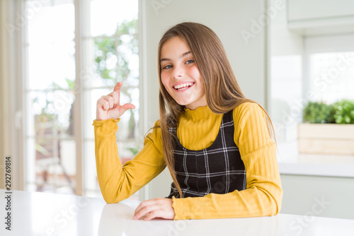 Young beautiful blonde kid girl wearing casual yellow sweater at home smiling and confident gesturing with hand doing small size sign with fingers looking and the camera. Measure concept. Free Download Young beautiful blonde kid girl wearing casual yellow sweater at home smiling and confident gesturing with hand doing small size sign with fingers looking and the camera. Measure concept. - GFXLoad