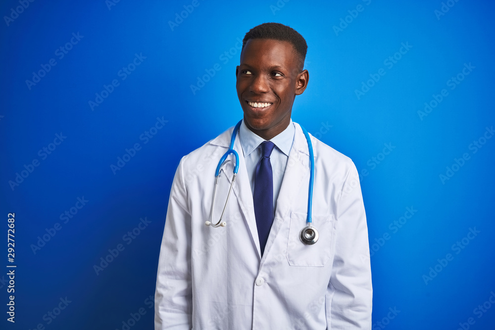 African american doctor man wearing stethoscope standing over isolated blue background looking away to side with smile on face, natural expression. Laughing confident. African american doctor man wearing stethoscope standing over isolated blue background looking away to side with smile on face, natural expression. Laughing confident.
